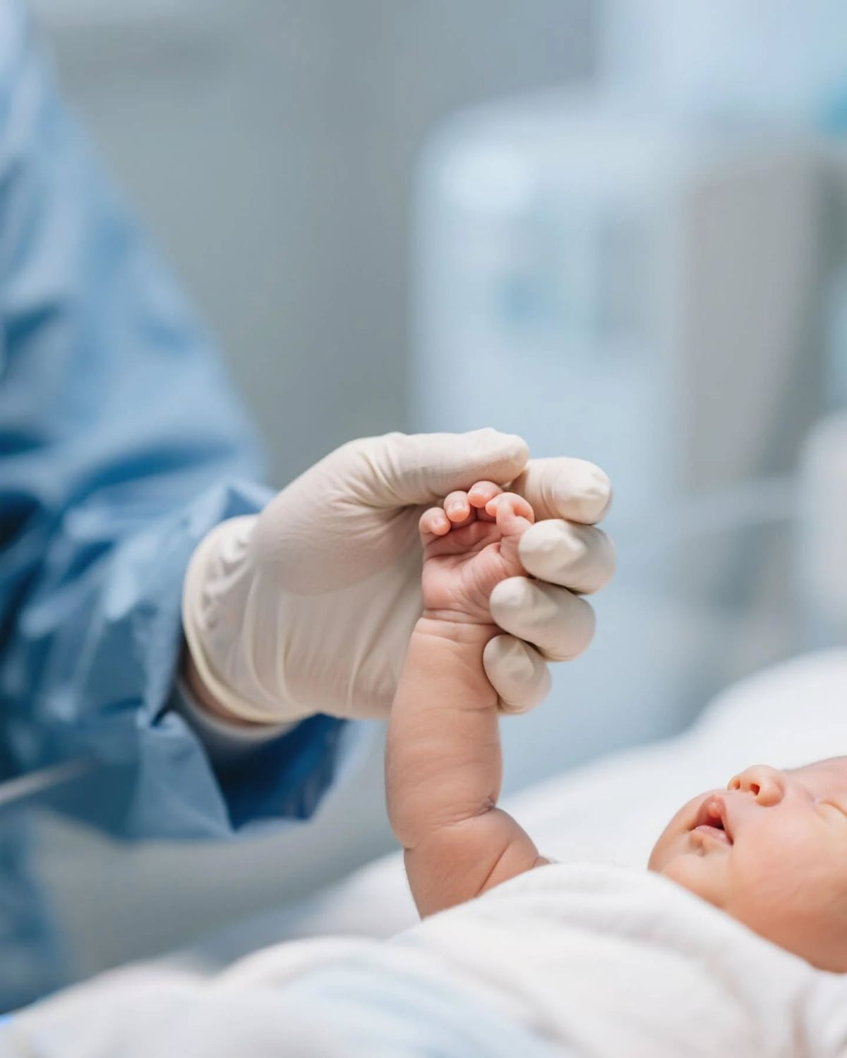 A clinician's gloved hand holding a newborn's hand